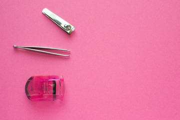 Woman make up equipment - tweezers, plastic eyelash curler and nail clippers on pink background. Copy space for text.