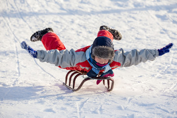 Fototapeta na wymiar happy boy riding at the sledge on snowy hill