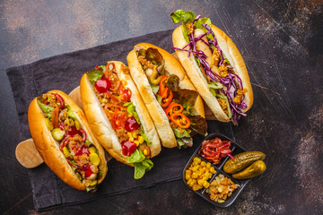 Hot dogs with assorted toppings on a dark background, top view.