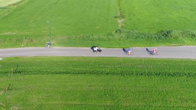 Aerial following a scooter driving over narrow rural road keeping up fast pace also showing passer-by traffic two cyclists beautiful green grass landscape on both side of street 4k high resolution
