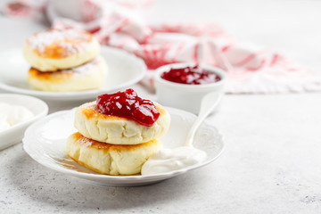 Cottage cheese pancakes with sour cream and jam on white plate.