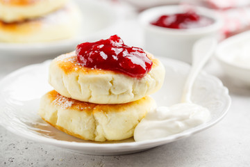 Cottage cheese pancakes with sour cream and jam on white plate.