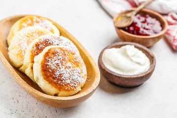 Cottage cheese pancakes with sour cream and jam on a wooden bowl.