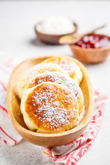Cottage cheese pancakes with sour cream and jam on a wooden bowl.