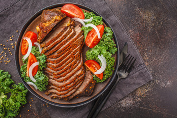 Spicy baked beef with kale salad in black plate on dark background.