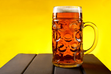 A glass, a mug of beer on a wooden table and an yellow background