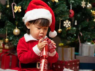 toddler baby girl wearing santa claus costume play in front of christmas tree