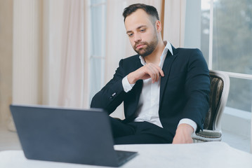 Hipster bearded businessman in suit with laptop on window background