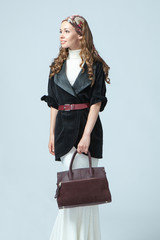 Stylish beautiful woman wearing a scarf on her head, holding a fashionable handbag in her hand. Studio photography on a blue background. Vertical orientation.