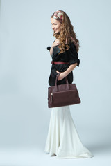 Stylish beautiful woman wearing a scarf on her head, holding a fashionable handbag in her hand. Studio photography on a blue background. Vertical orientation.