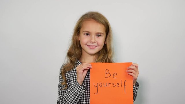 Happy girl showing handwritten words  Be yourself on the orange sheet