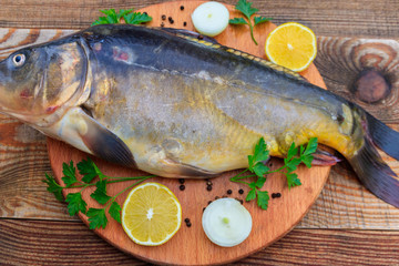 Raw carp fish with lemon, onion, pepper and parsley on cutting board on rustic wooden table