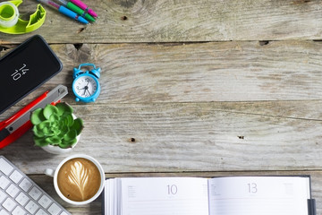 Office supplies, coffee and green plant on the left side of wooden background 