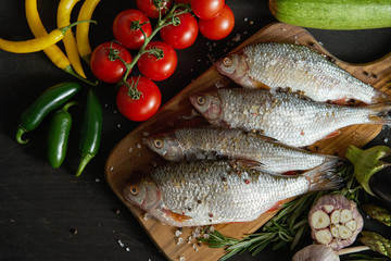 top view of four fresh raw dorada fish on a wooden board with a set of vegetables on a black table