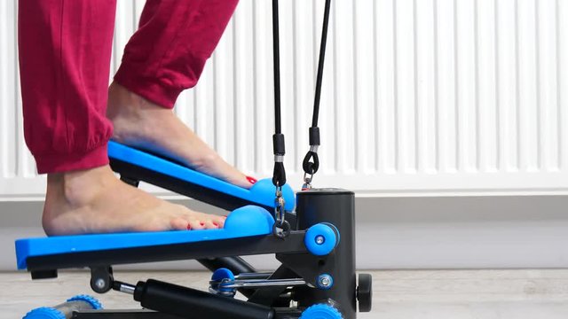 Woman doing exercises at home on stepping machine. Female legs foot on stepper trainer