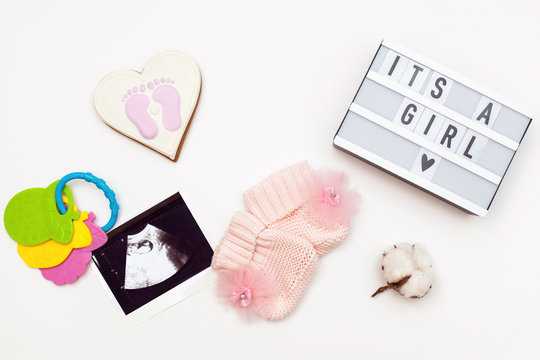 flatlay pregnancy composition with space for text. top view of children's accessories: toys, pacifier, baby screen, baby projector lamp "it's a girl", a cotton flower and delicious gingerbread