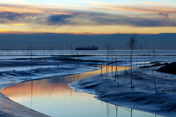 das Wattenmeer an der Nordseeküste bei Sonnenuntergang mit Frachtschiff in der Ferne