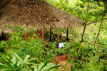 Thatched roof cottage in remote place in exotic tropical Thai natural forest. Some clothes hanging and drying in air.
