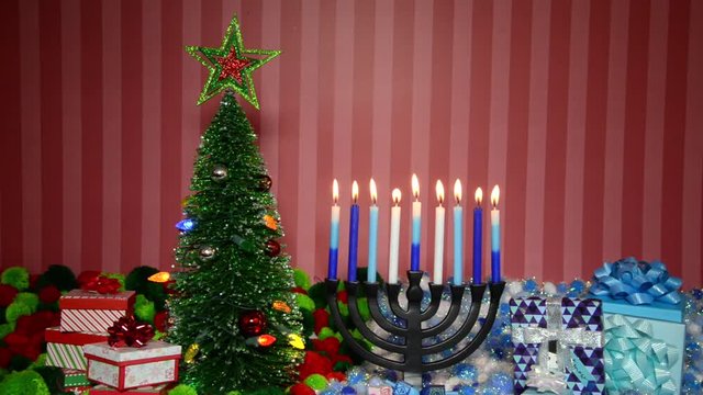HD Video Christmas tree with presents next to Hanukkah menorah burning candles, dreidel, and gifts with yarn balls in holiday colors. Many multi faith families celebrate both Xmas and Hanukkah.