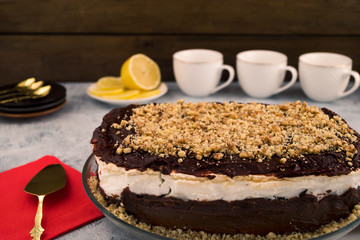 The cake is chocolate with walnuts. Dishes for dessert. Ground nut. Wooden background. Sliced lemon.