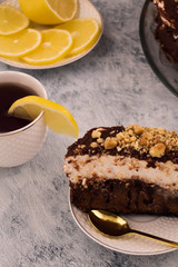 Chocolate dessert on a plate. Brown and white cake. Vertical. A slice of lemon on a Cup of tea. Sliced lemon on a plate. Wooden background.