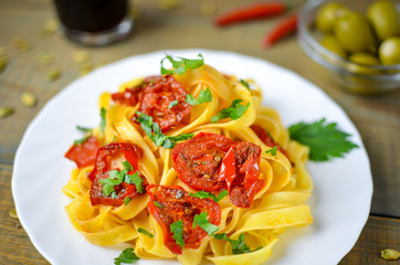 Spaghetti with grilled tomatoes and herbs. Mediterranean lunch with red wine. Wooden table with olives and hot red pepper.