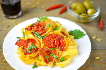 Spaghetti with grilled tomatoes and herbs. Mediterranean lunch with red wine. Wooden table with olives and hot red pepper.