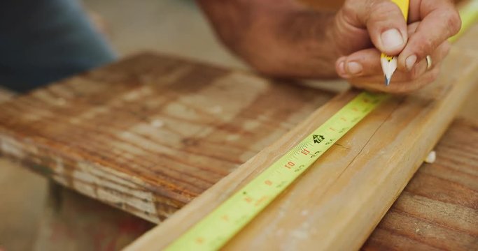 Skilled carpenter carefully measures and marks lengths on wood