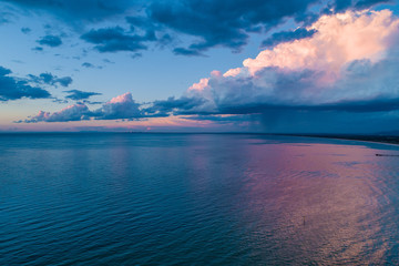 Rain and stormy clouds approaching the ocean coastline and beautiful sunset - aerial view