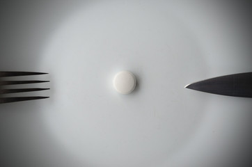 Pills in a white plate with fork and knife. The concept of imposing drugs.