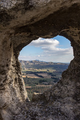 Fototapeta na wymiar The valley between Les Baux de Provence and the Alpilles mountains are dotted with farms as viewed through a natural frame in the wall