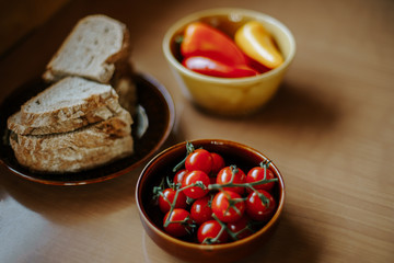 Eine Schüssel Kirschtomaten und eine Schüssel Paprika, sowie ein Teller geschnittenes Brot auf einem Tisch
