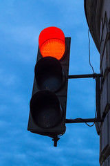 Red traffic light in the blue evening sky on the wall of a building in the city at dusk