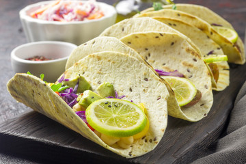 Healthy corn tortillas with chickpeas, tomatoes, avocado, fresh arugula, limes over dark background, top view. Healthy food, gluten-free, allergy-friendly, weight loss concept