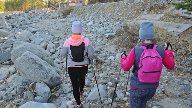 Woman do Nordic walking in nature near mountain river. Girls and children use trekking sticks and nordic poles, backpacks. Family travels sports. Kid is learning from mother and grandmother the proper