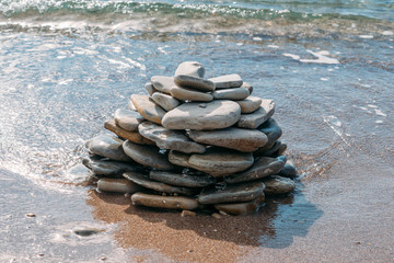 Stone tower on sea coast or beach near water on sand, summer inspiration background