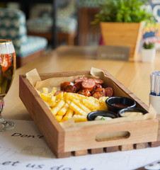 Delicious smoked sausage with chips, french fries with sauce on wooden board. street fast food festivel concept. roasted meat and cold beer drinks.stylish service.