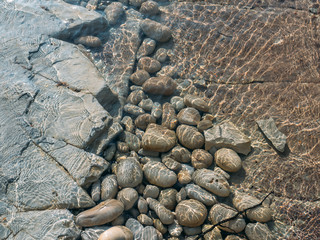 Rock stones at sea beach with clear water texture, summer natural background