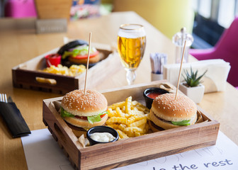 One black colored and two normal small mouth-watering, delicious burgers on the wooden tray served with red ketchup sauce and beer.