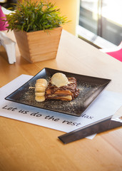 Chocolate Waffle topped with ice cream and banana decoration on black plate