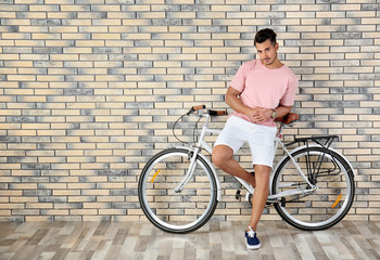 Fototapeta premium Handsome young hipster man with bicycle near brick wall