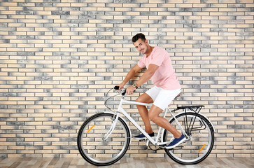 Fototapeta premium Handsome young hipster man riding bicycle near brick wall