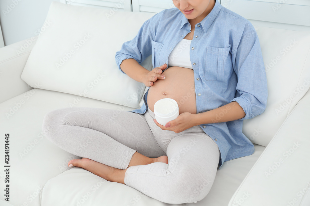 Poster Pregnant woman applying body cream on belly at home, closeup