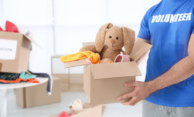 Male volunteer holding box with donations indoors. Space for text