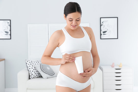 Pregnant woman holding body cream at home