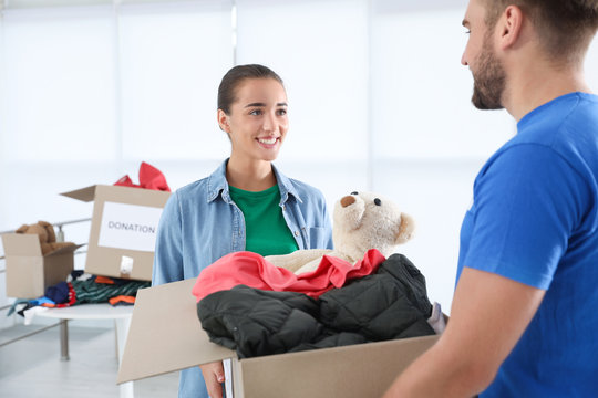 Young woman giving box with donations to male volunteer indoors