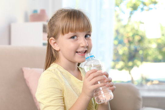 Cute little girl holding bottle with water indoors