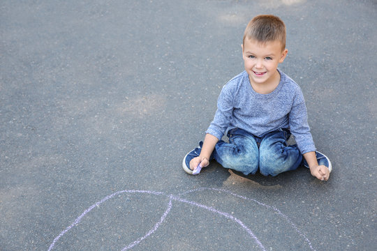 Little child drawing with colorful chalk on asphalt. Space for text