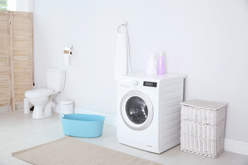 Modern washing machine in light bathroom interior