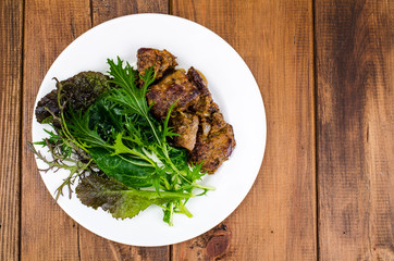 Slices of fried liver, green leaves of salads